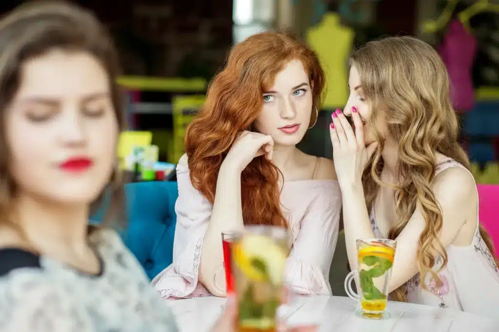 Woman whispering to another woman behind a third woman