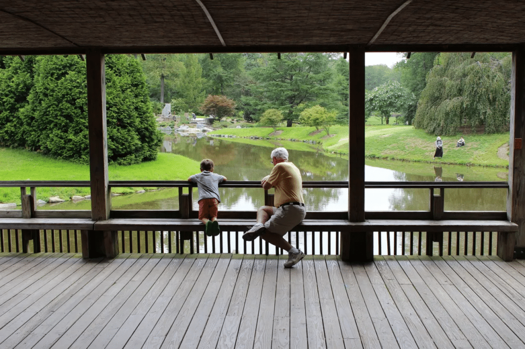 Little boy and grandpa sitting on a bridge overlooking river