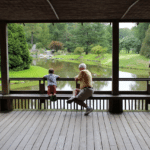 Little boy and grandpa sitting on a bridge overlooking river