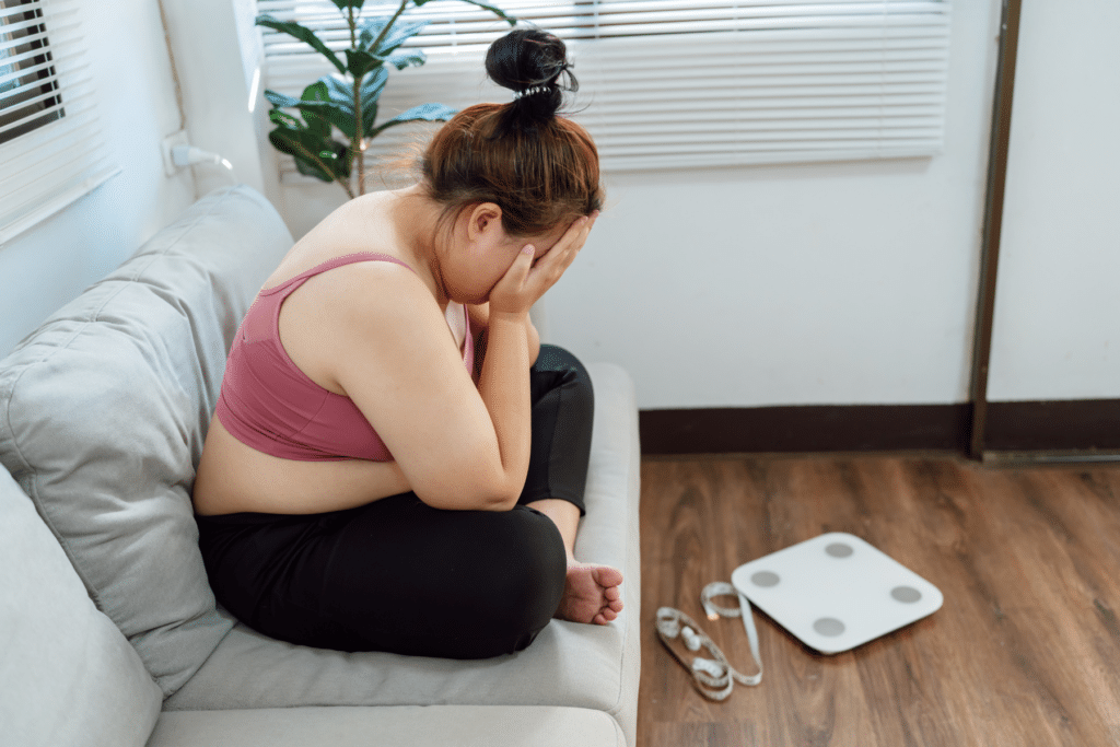 woman sitting covering her face next to a scale