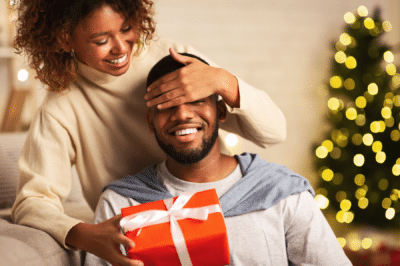 wife covering husband's eyes and surprising him with a Christmas gift