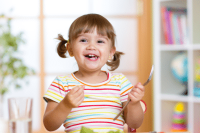 Toddler smiling and eating her veggies