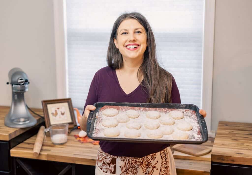 woman smiling holding a cookie sheet full of powdered cookies