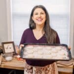 woman smiling holding a cookie sheet full of powdered cookies