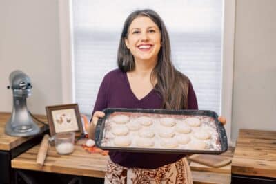 woman smiling holding a cookie sheet full of powdered cookies
