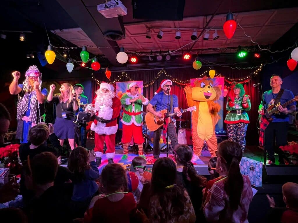 SQRRL! several people on lit stage playing instruments and singing in Christmas costumes and a squirrel