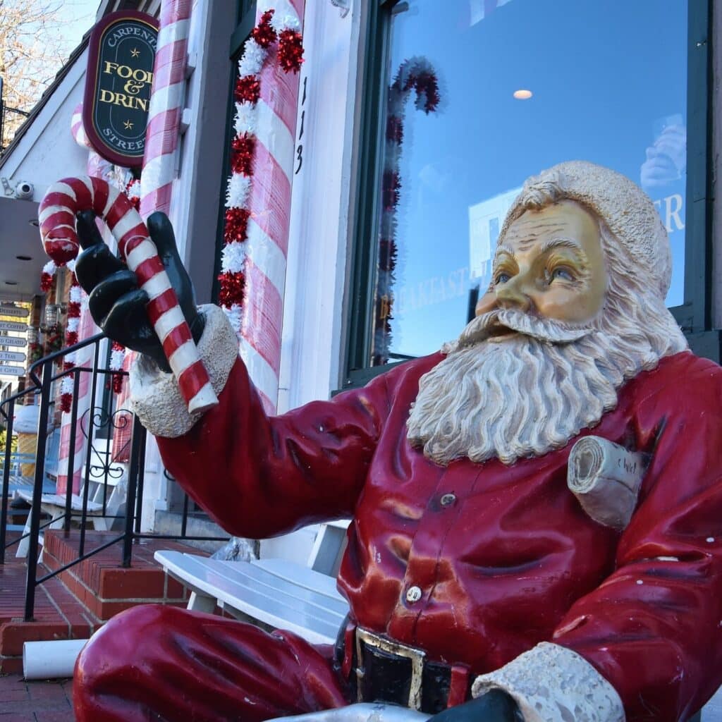 A Santa statue sitting on a bench holding a candy cane outside