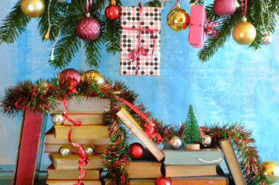 stacks of books under a pine tree and Christmas ornaments strewn over the books
