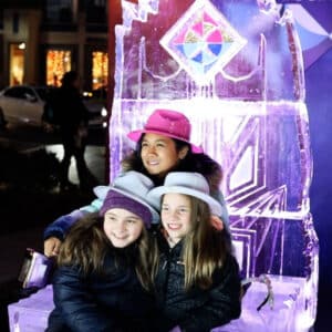 Mom and 2 girls smiling sitting on an ice sculpture chair