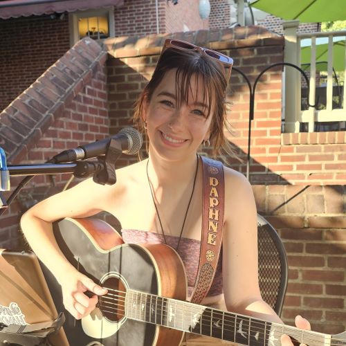 young, redheaded, smiling white woman with acoustic guitar slung around one shoulder