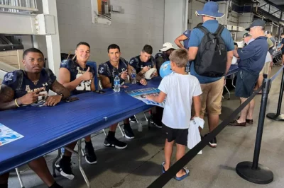 Navy football players sit at a long table greeting fans
