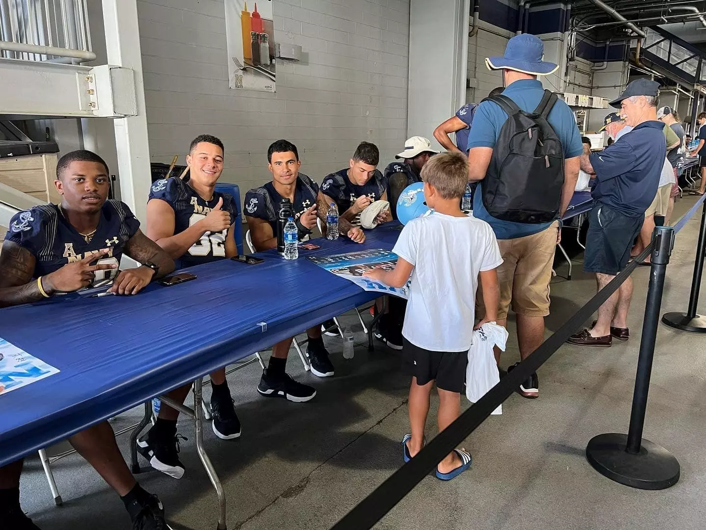 Navy football players sit at a long table greeting fans