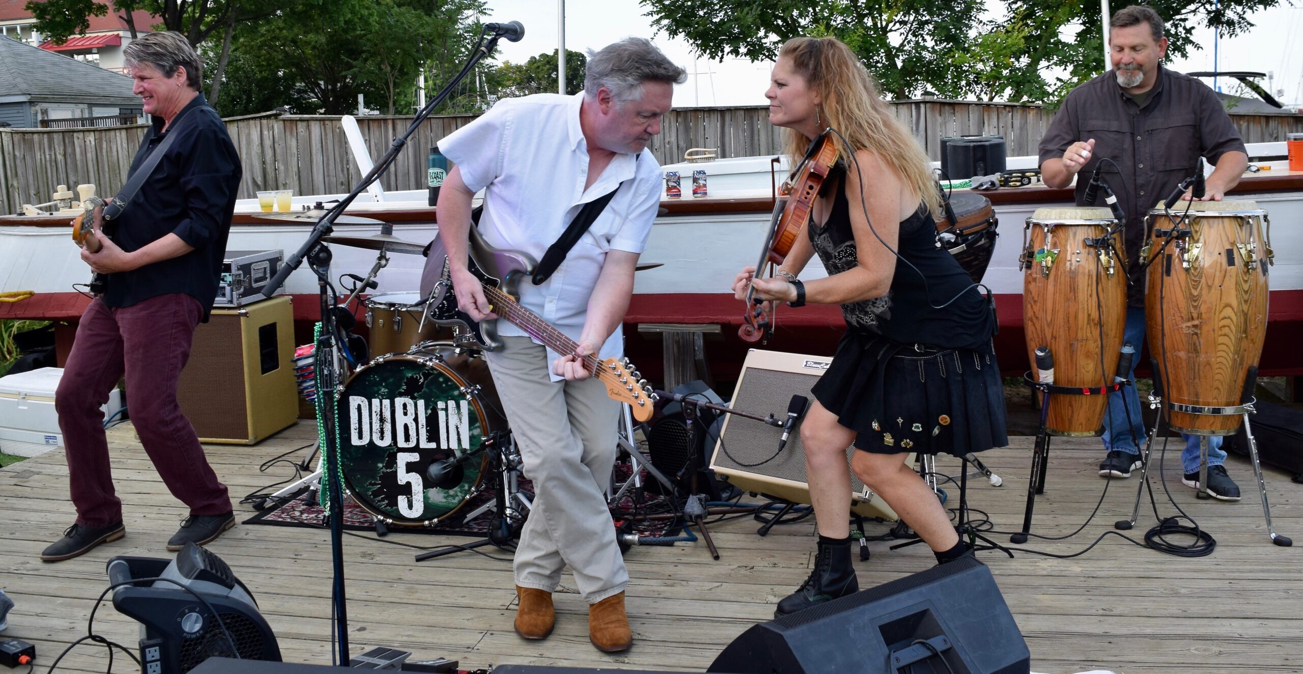 a white man in a white shirt plays an electric guitar and a white woman in a black tank top and skirt plays a fiddle