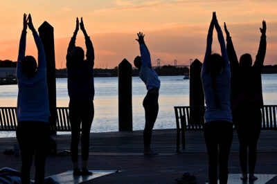 A photo of people doing yoga at Yoga on the Dock with a sunrise in the background.