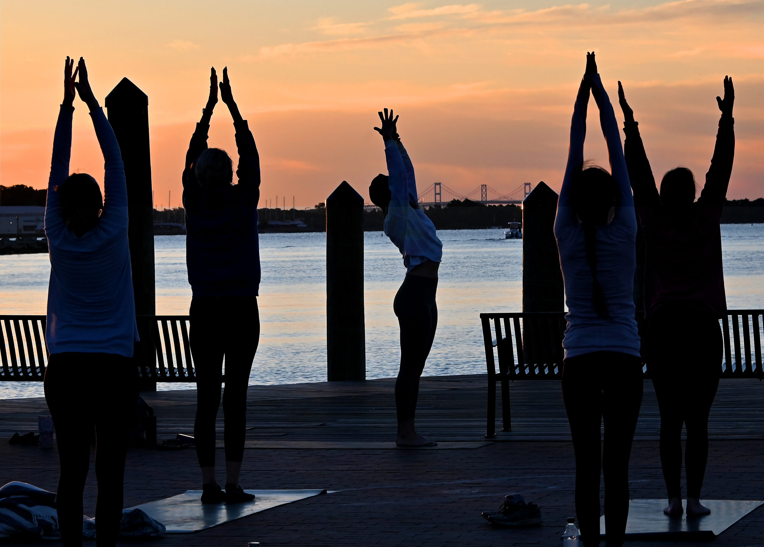 A photo of people doing yoga at Yoga on the Dock with a sunrise in the background.