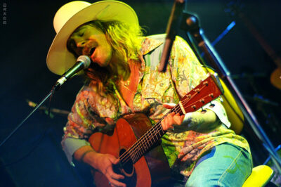 An image of Donavon Frankenreiter with a cowboy hat, guitar, and microphone.