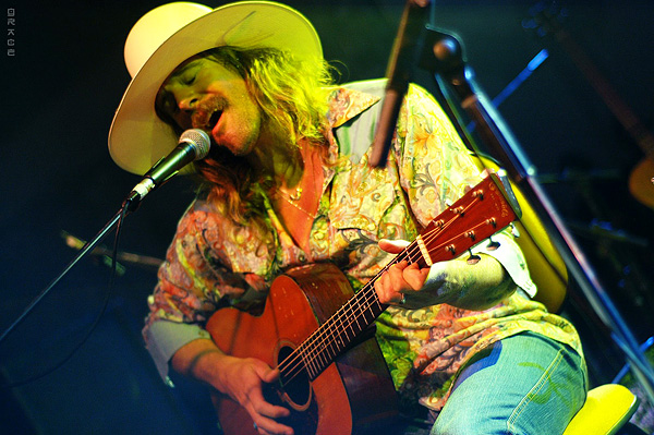 An image of Donavon Frankenreiter with a cowboy hat, guitar, and microphone.
