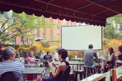 People sit at tables looking at a screen projector outside at Reynolds Tavern for their Dinner and a Classic event.