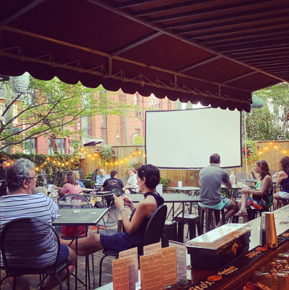 People sit at tables looking at a screen projector outside at Reynolds Tavern for their Dinner and a Classic event.