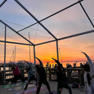 A group of people doing yoga with a sunrise as the background at Sunrise Dock Yoga with Fount.