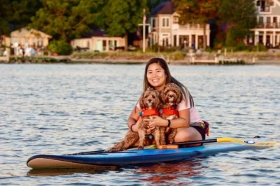 An image of a girl on a kayak with her dog in a life vest during Capitol SUP's Yappy Hour.