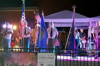 American Legion's Independence Day Celebration. Men on a stage are lined up holding American flags at night.