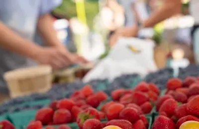 An image of strawberries in cartons at the Farragut Farmer's Market with people that are blurred in the background.