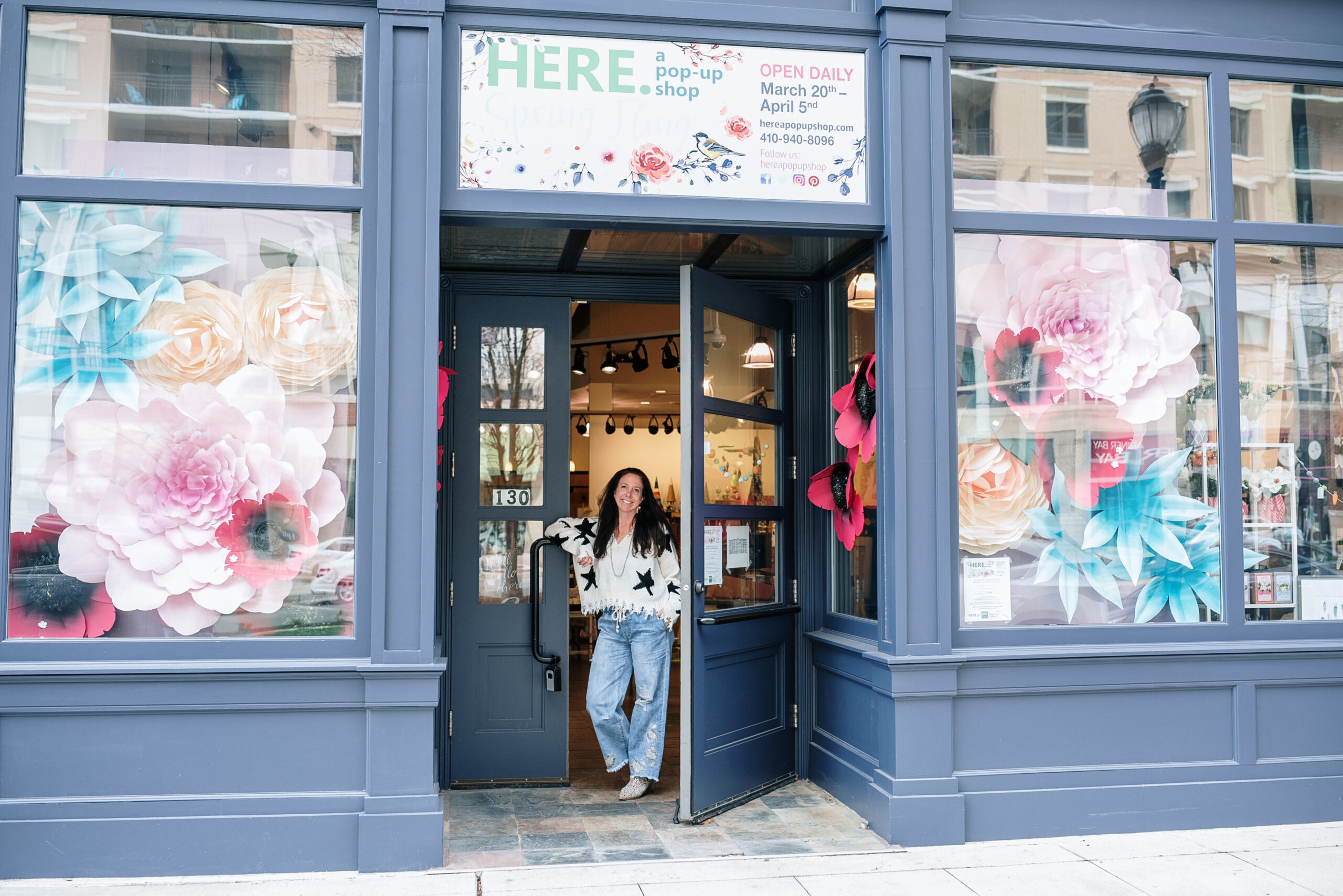 A photo of the owner of HERE. a pop up shop standing in front of her store, waiting for the Charm Bar + happy hour to start.