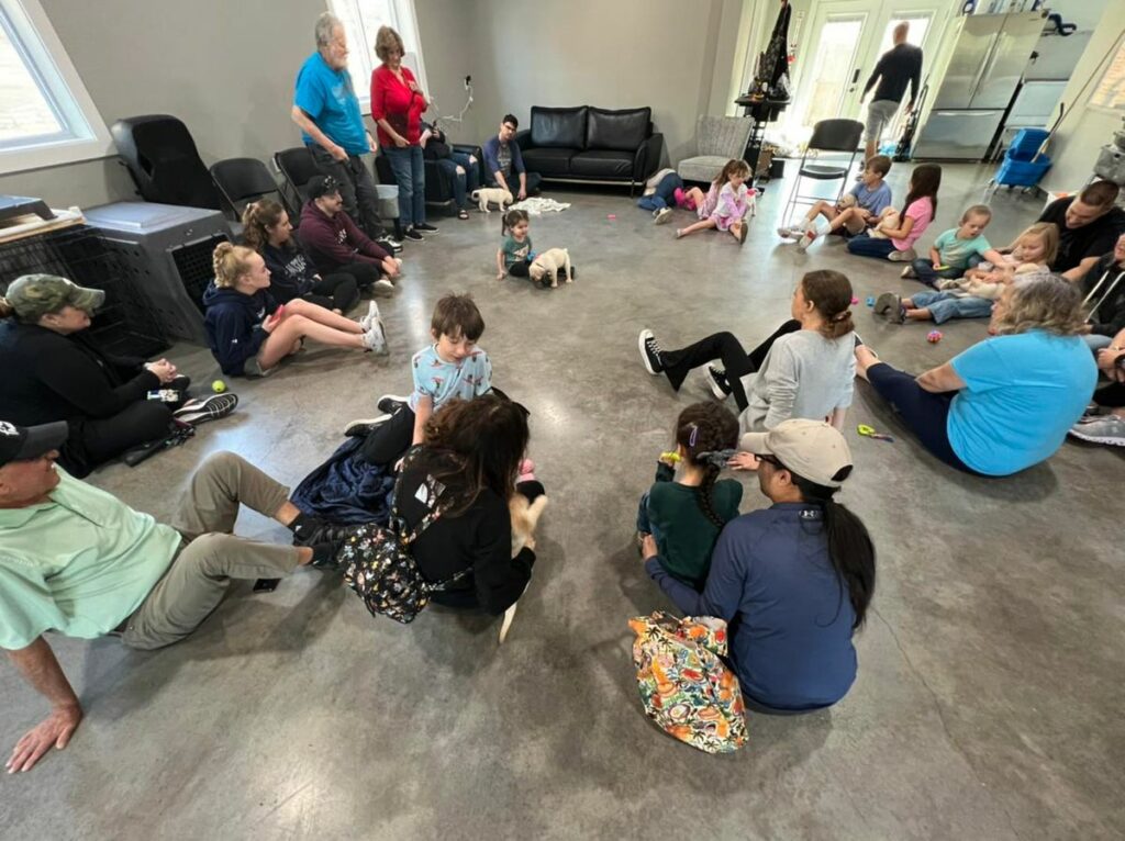 A group of kids and adults sitting on the floor with multiple puppies at Puppies & Pizza.
