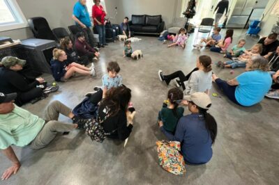 A group of kids and adults sitting on the floor with multiple puppies at Puppies & Pizza.