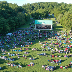 ariel view of group of people sitting on lawn watching an orchestra