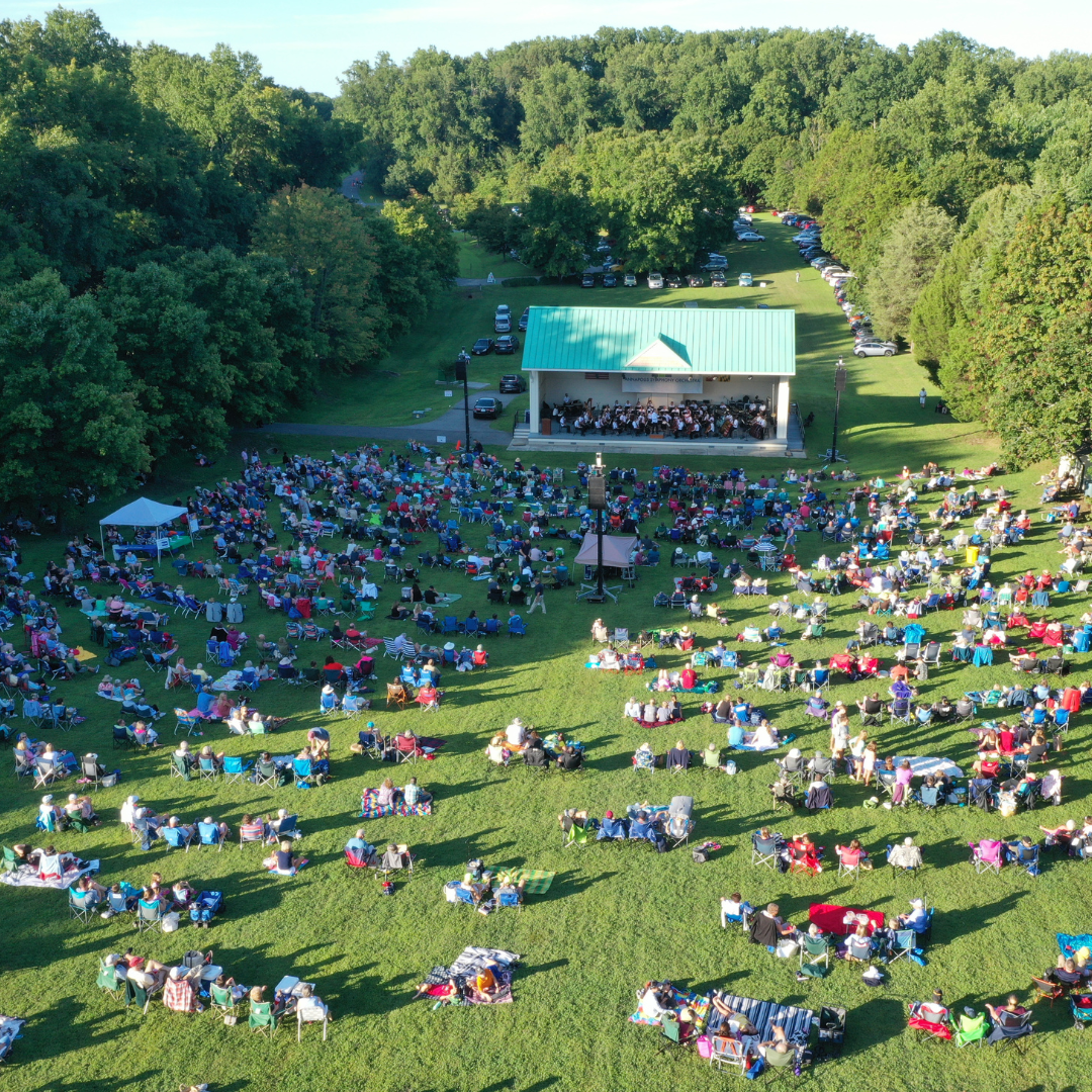 ariel view of group of people sitting on lawn watching an orchestra