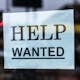 Close-up of a Help Wanted sign taped to a glass window in a storefront.